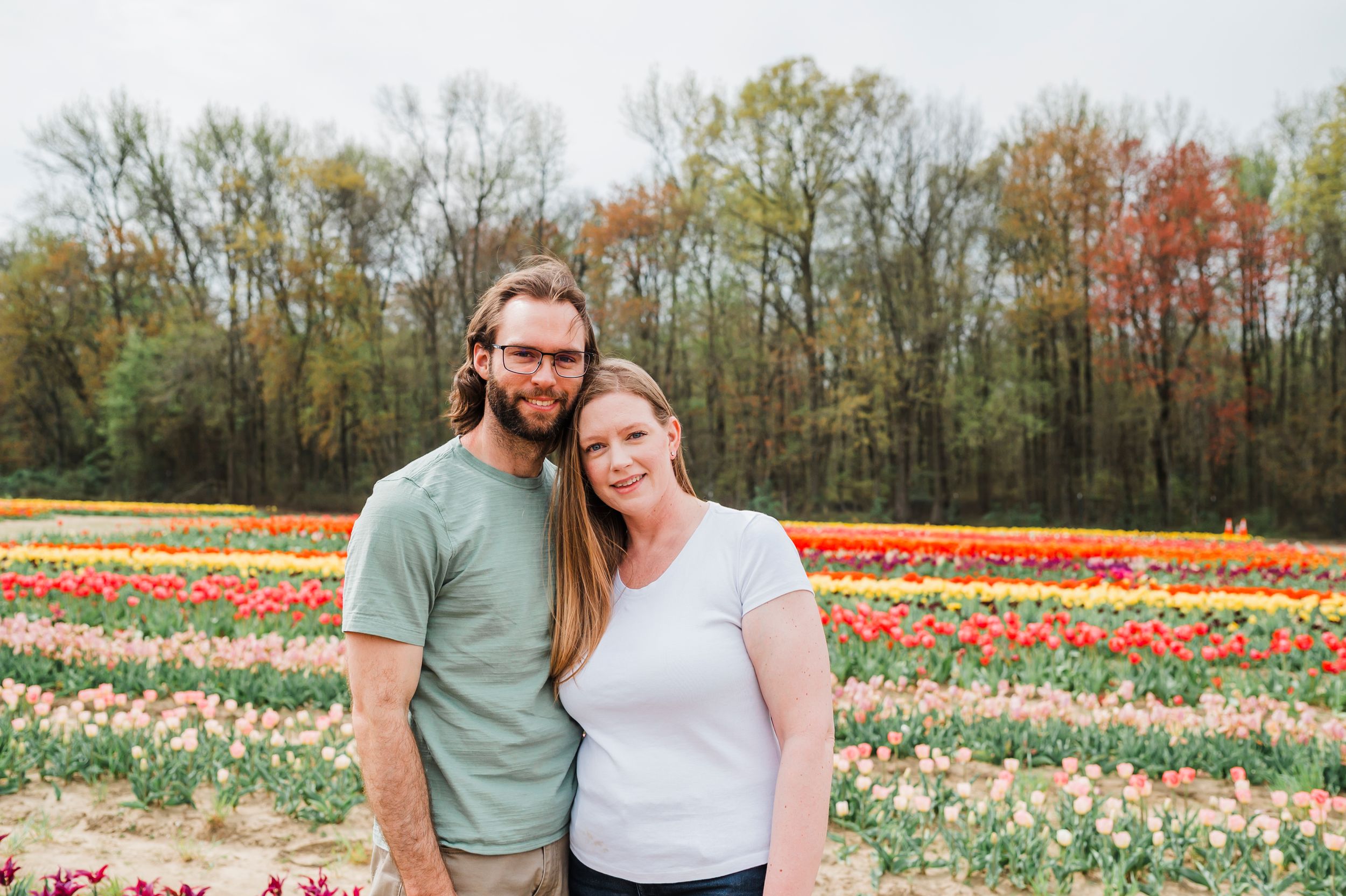 A couple stands in a vibrant tulip field during spring with colorful flowers in full bloom.