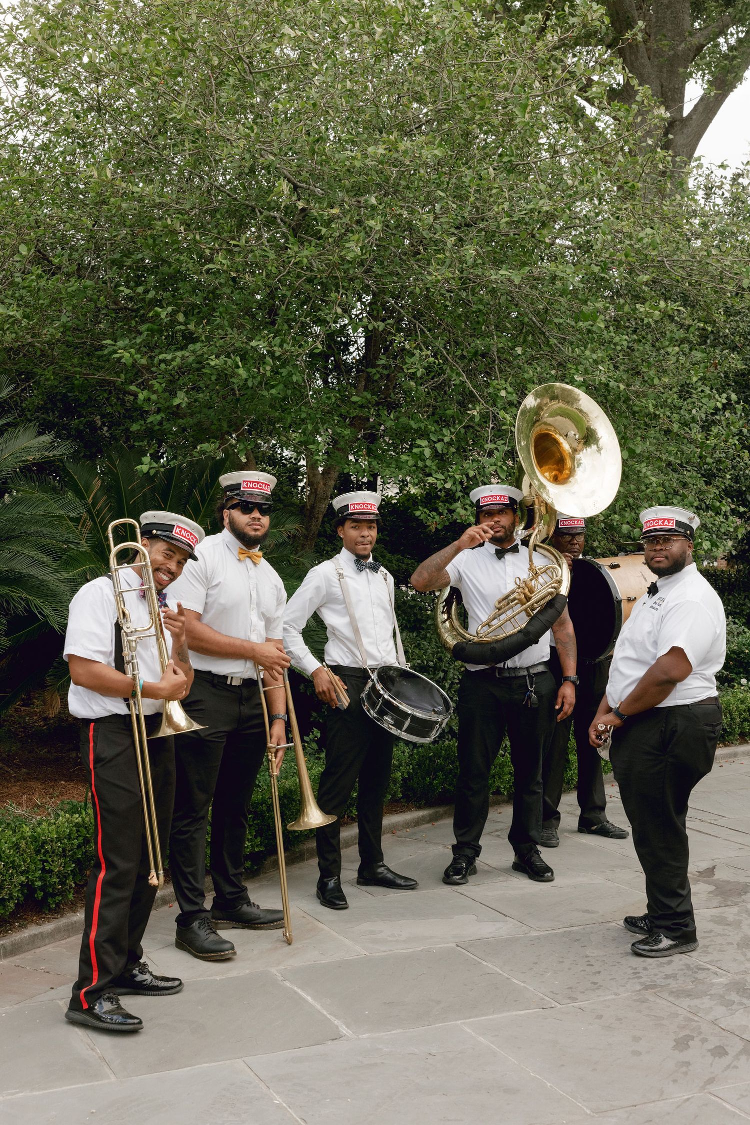 A brass band wearing traditional uniforms performs while standing in a curved formation outdoors.