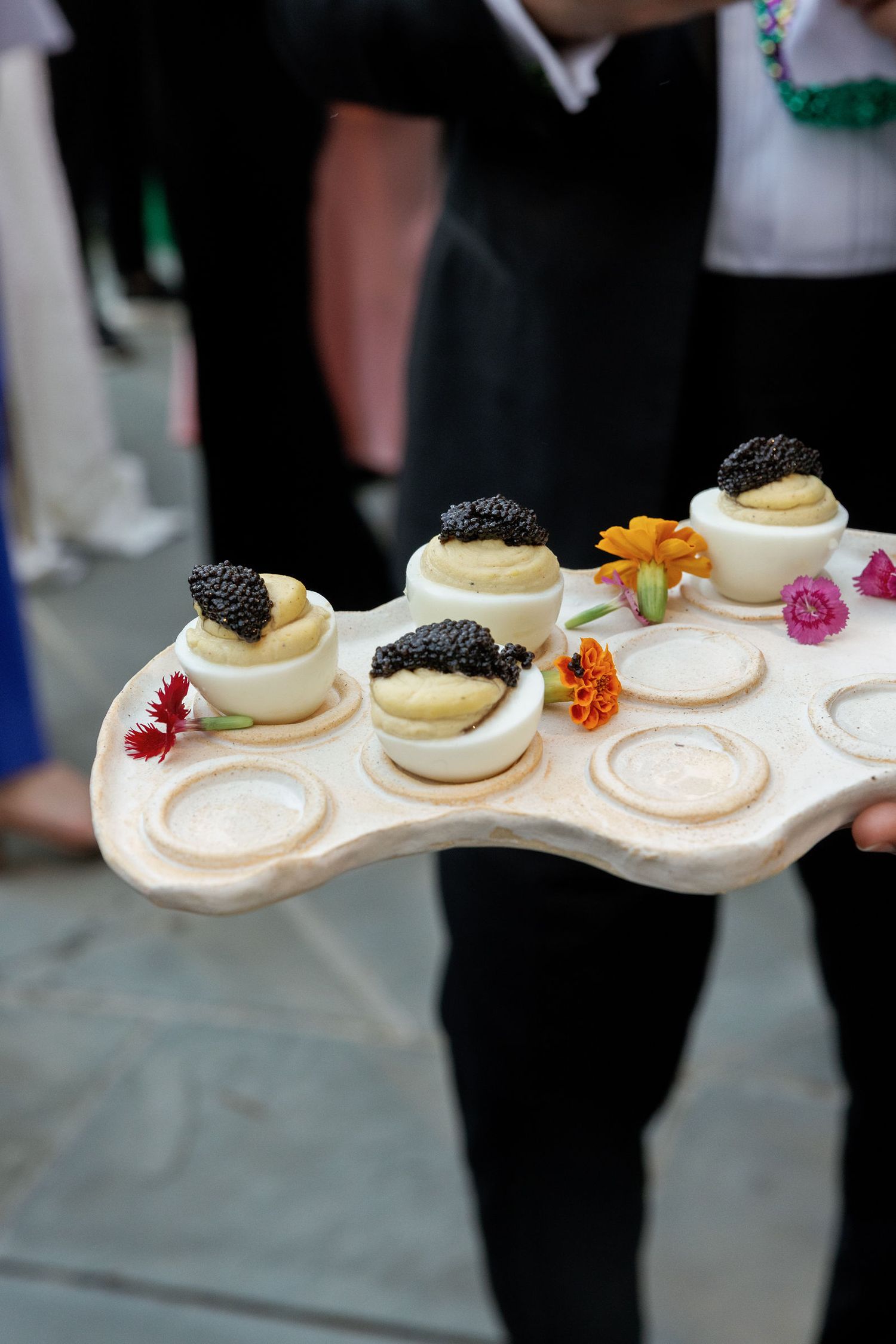 Elegant deviled eggs topped with caviar and edible flowers served on a curved white serving platter at an upscale event.