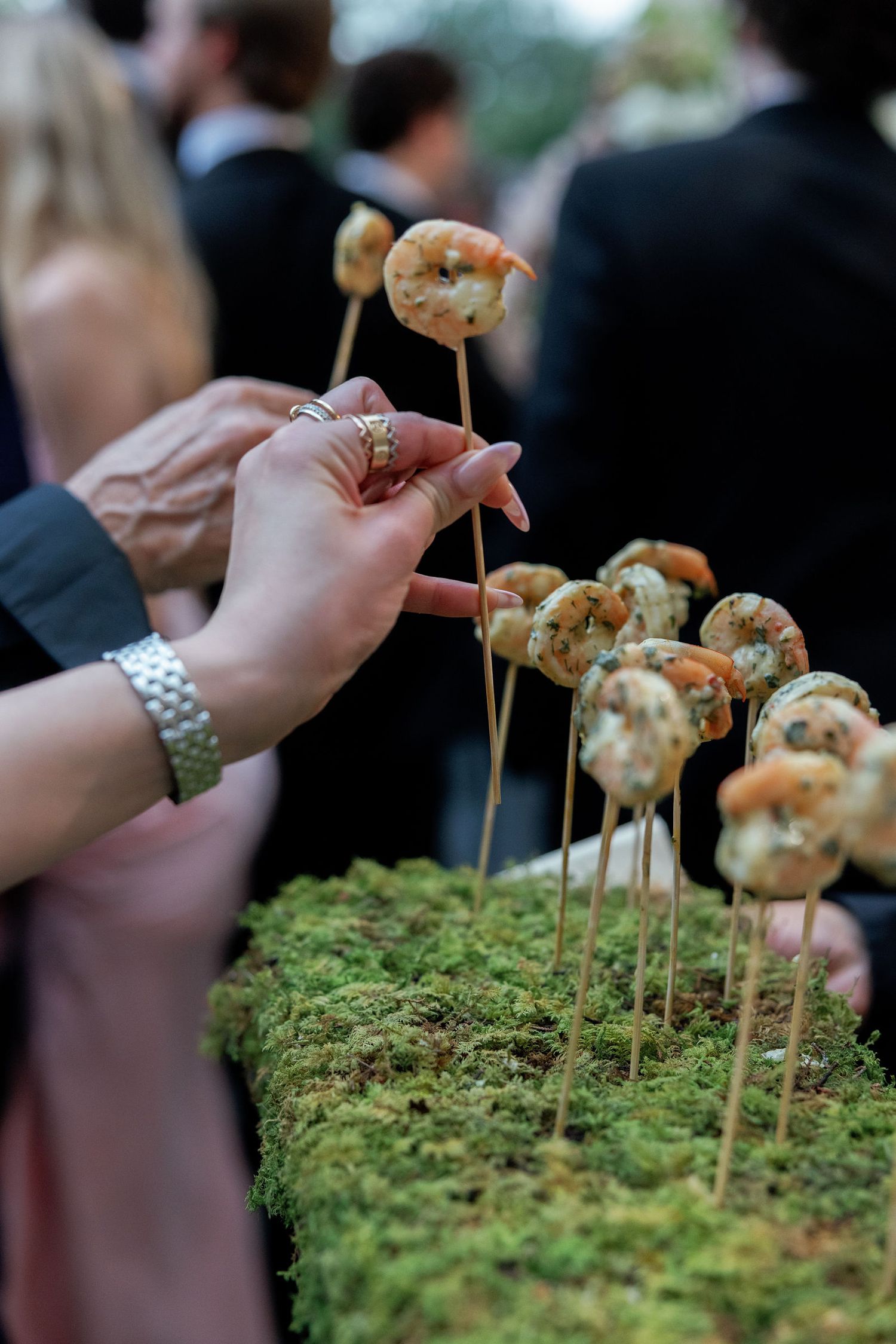 Grilled shrimp appetizers arranged on moss with bamboo skewers being served at an upscale outdoor event.