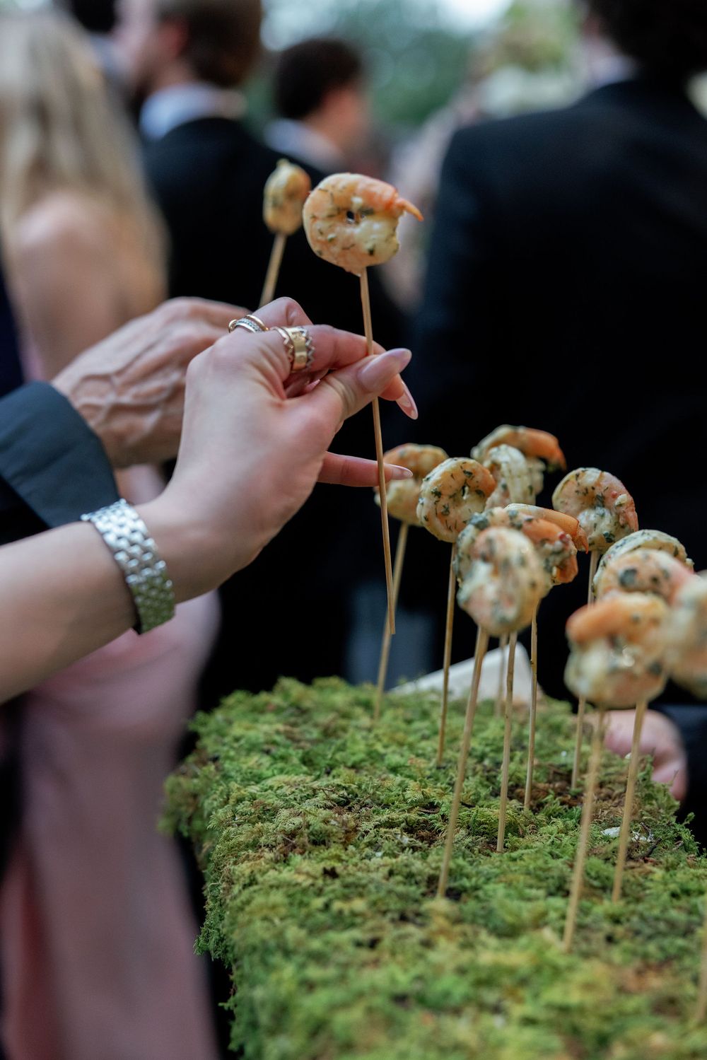 Grilled shrimp appetizers arranged on moss with bamboo skewers being served at an upscale outdoor event.