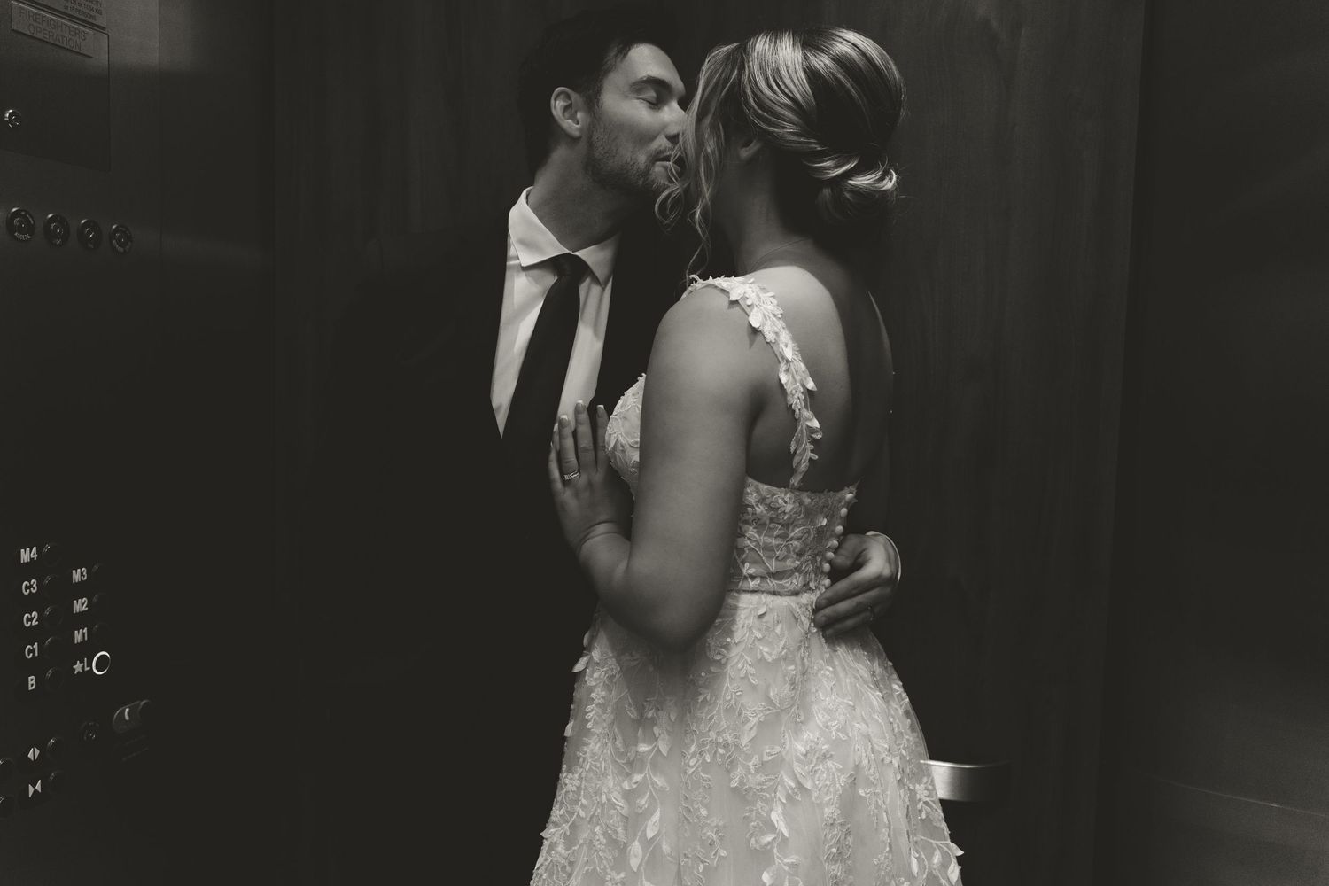 Black and white photo of wedding couple embracing in dramatic lighting.