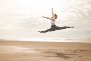 Graceful dancer performs dramatic split leap on sandy beach at sunset.