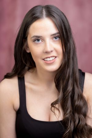 Portrait of a young woman with long dark hair and bright smile wearing a black tank top against a rosy background.