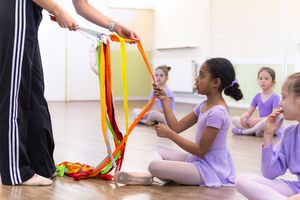 Young students in purple leotards participate in a dance class with colorful ribbons during instruction.