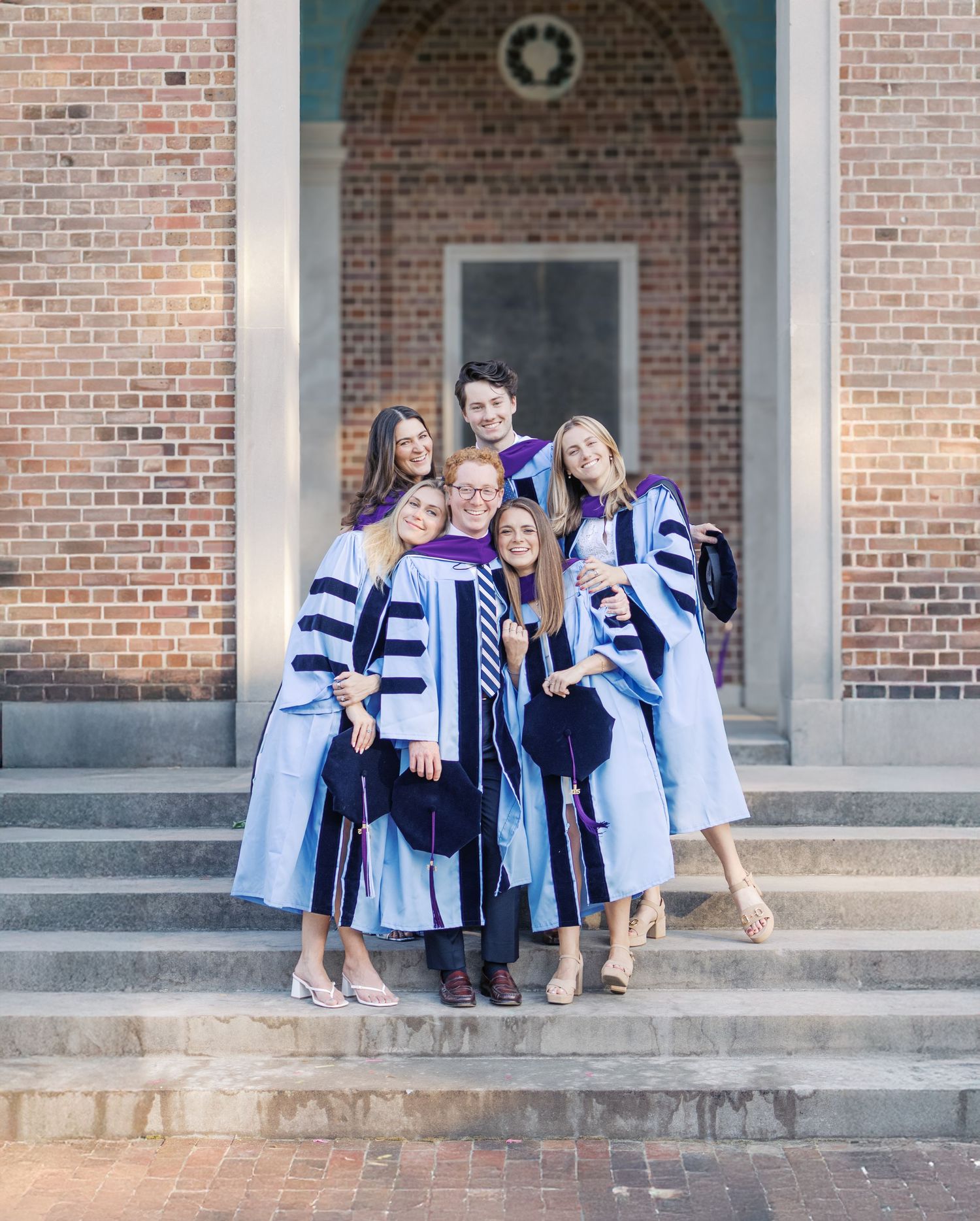 A group in matching graduation robes and stoles posing on brick building steps.
