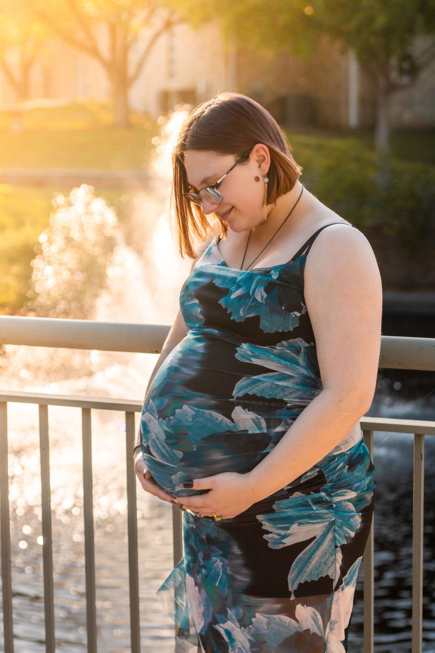 Radiant expectant mother in flowing dress, holding her belly with love and joy during a warm, dreamy outdoor maternity session.