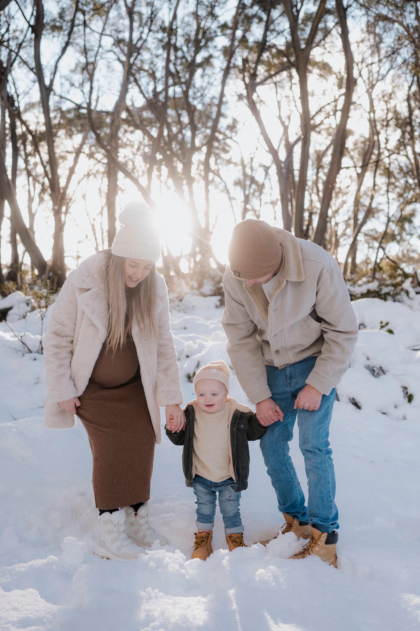 Three people enjoying a winter day together in snowy woods with sunlight streaming through bare trees.