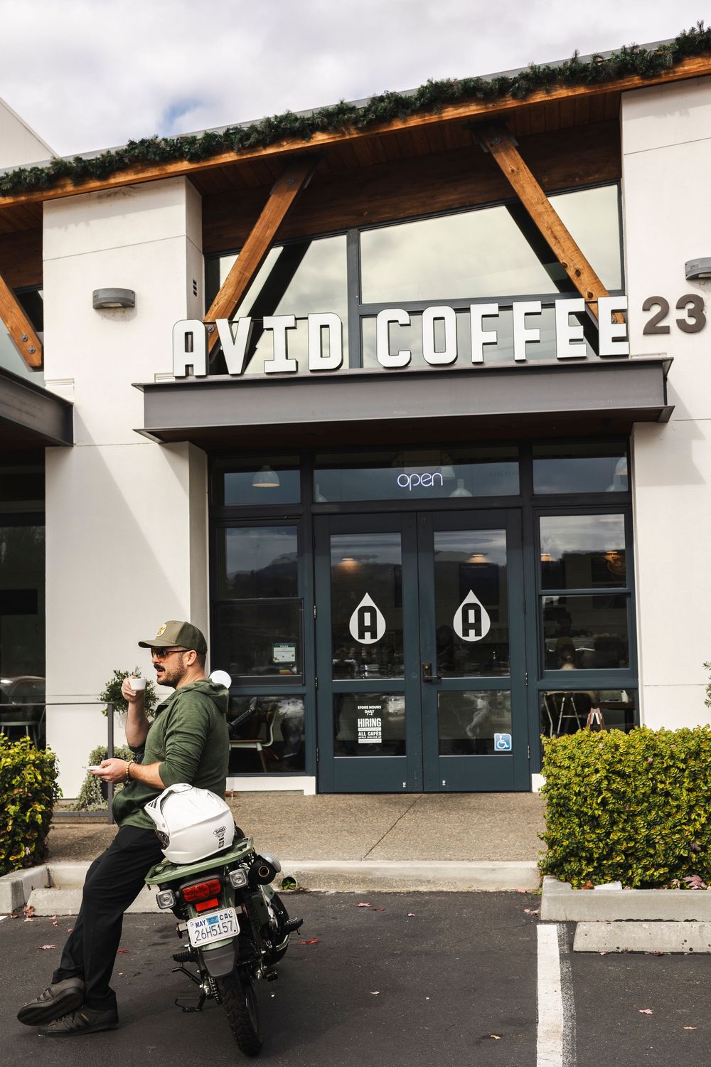 Modern coffee shop storefront with white exterior, wooden beams, and a motorcycle parked outside.