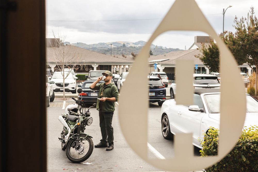 A law enforcement officer stands next to a motorcycle in a parking lot with mountains visible in the background.