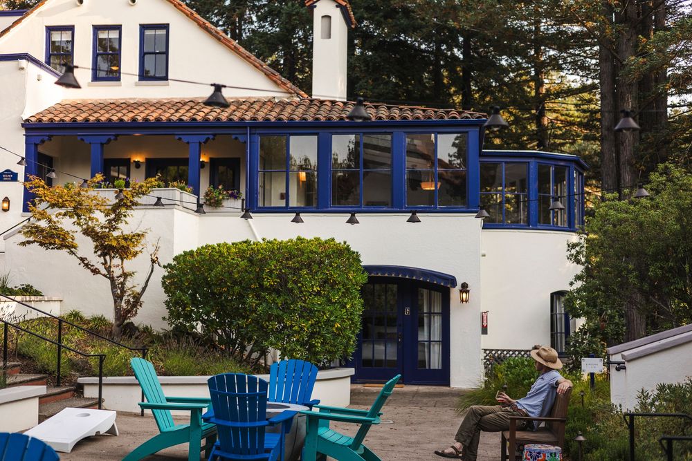 Coastal cottage with white walls and blue trim features outdoor seating areas overlooking a scenic garden landscape.