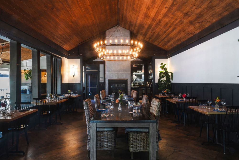 A modern restaurant interior with wood-paneled ceiling, pendant lighting, and dark furnishings creates an elegant ambiance.