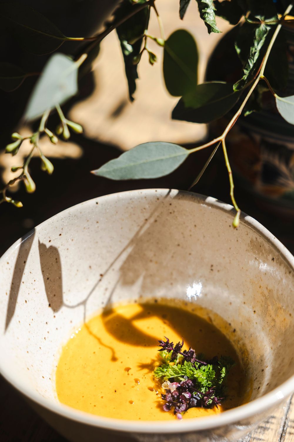 A series of bowls showing the progression of garnishing a vibrant yellow butternut squash soup with fresh herbs.