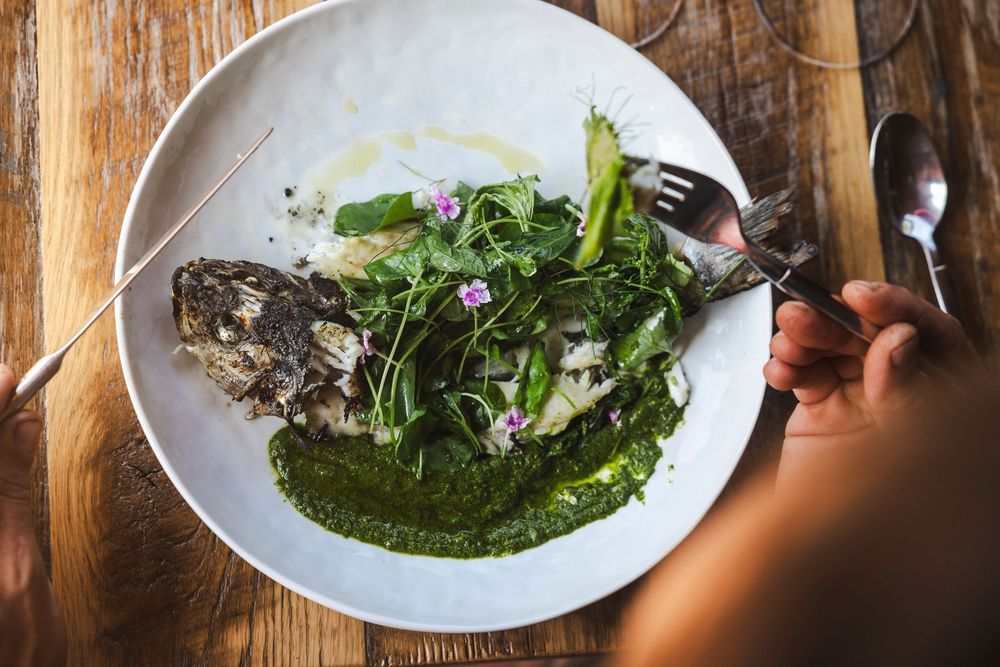 A series of plated dishes being garnished with microgreens and sauces on a rustic wooden surface.