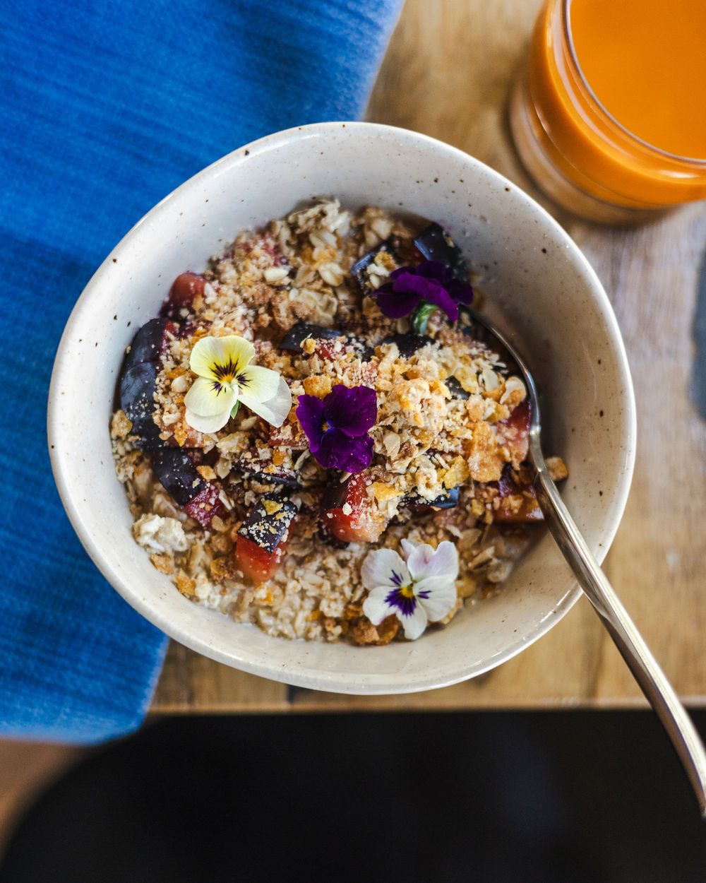 A series of white bowls filled with granola and fresh fruit garnished with purple edible flowers on a blue background.