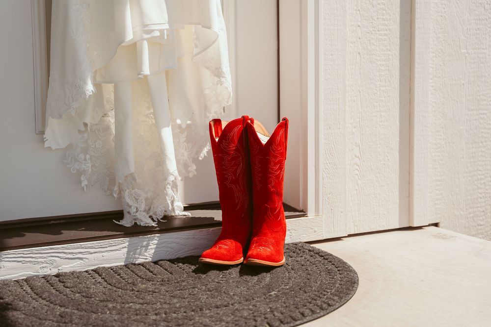 White wedding dress hemline contrasts beautifully with vibrant red cowgirl boots on a light floor.