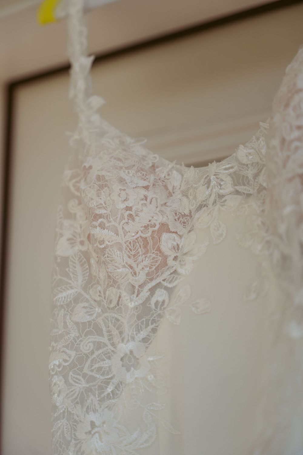 Detailed view of intricate white lace pattern on a wedding dress hanging against a neutral background.
