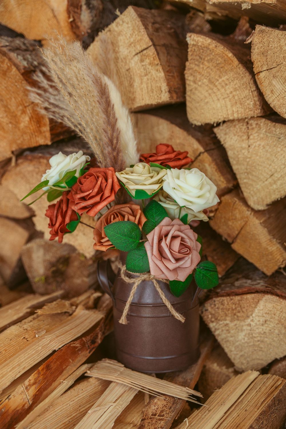 Rustic arrangement of pink and white roses in brown vase against stacked firewood background.