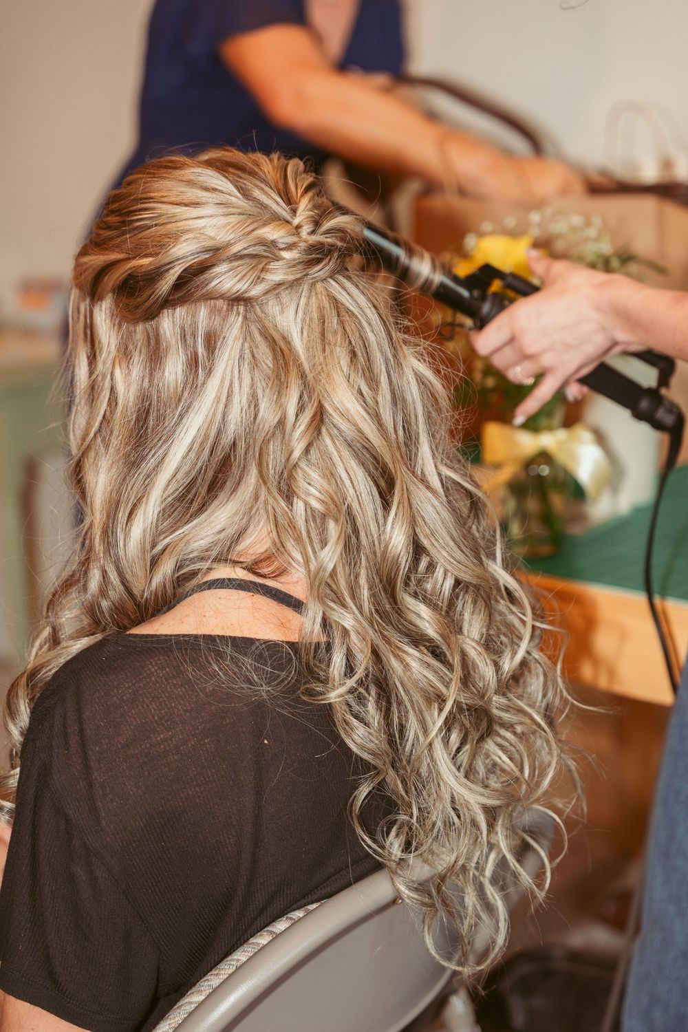 Professional stylist creating loose curls in long blonde hair with a curling iron.