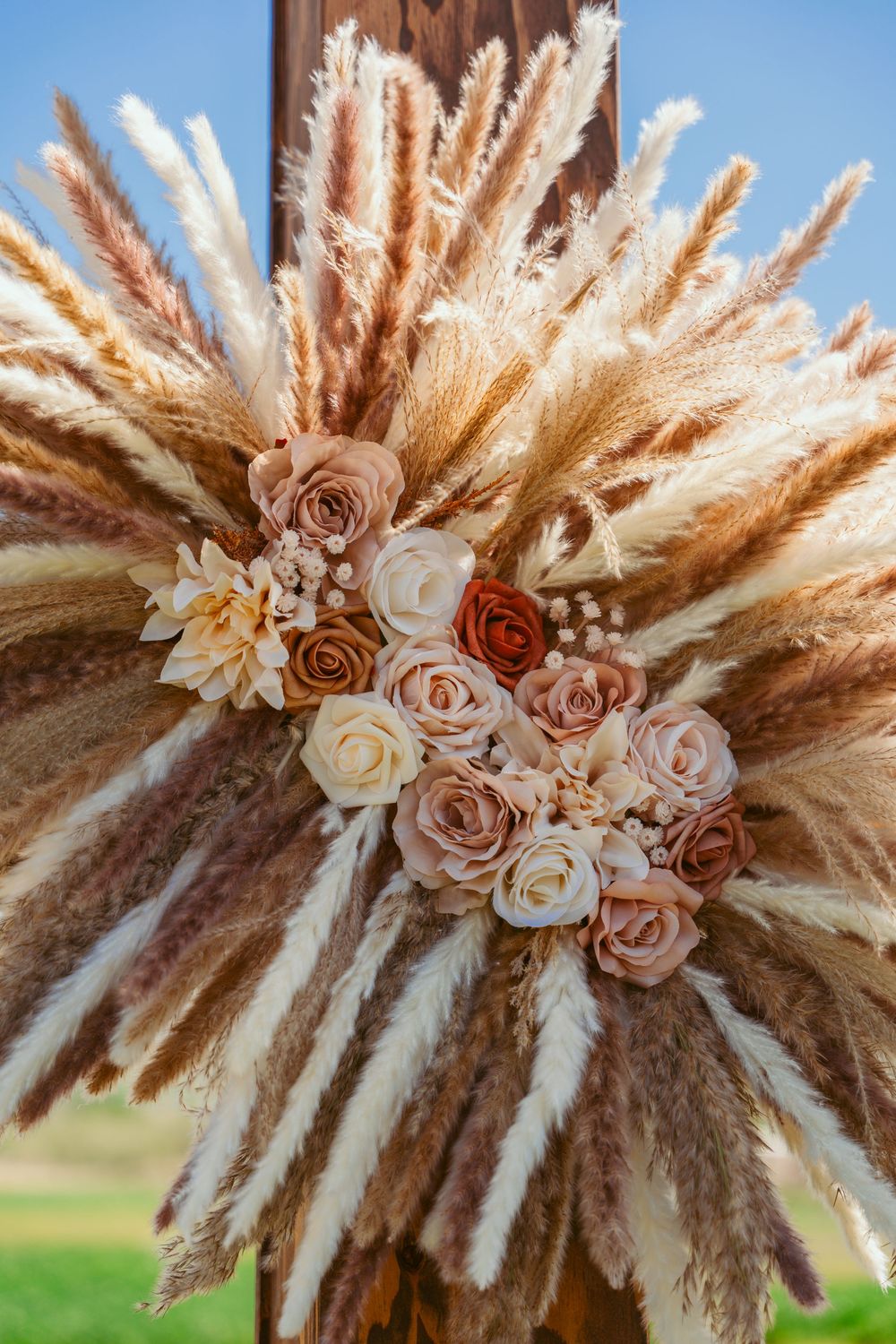 Romantic boho wedding wreath with dried pampas grass and blush roses on wooden backdrop.