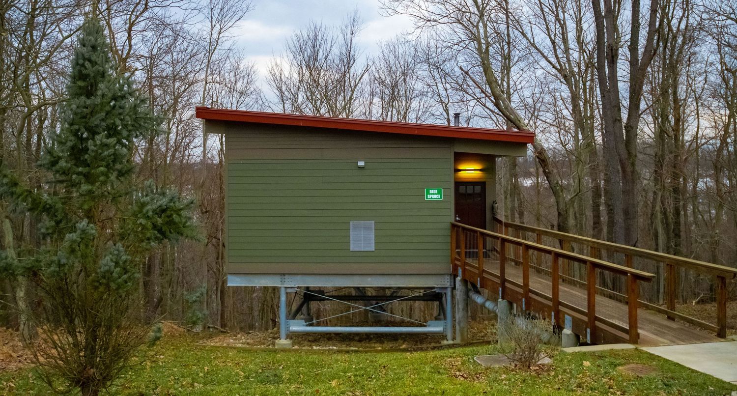A brown and green shelter building along a wooded hiking trail in a state park during autumn.