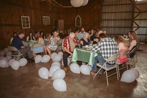 Wedding reception guests seated on the floor with white balloons scattered throughout a rustic barn venue.