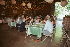 Reception guests dine at mint green tables under rustic wooden ceiling decorated with paper lanterns and string lights.