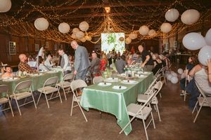Indoor party setup with mint green tablecloths, white paper lanterns, and string lights decorating a rustic barn venue.