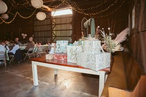 Gift table with wrapped presents and decor underneath string lights at rustic barn wedding reception.