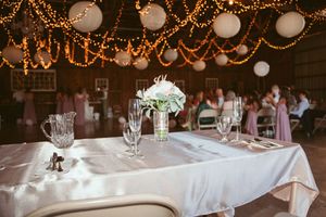 Elegant wedding table setting with white linens and floral centerpiece under romantic string light decor.