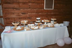 Dessert table with various treats displayed on white tablecloth against wooden barn wall.