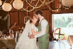 Couple sharing an intimate moment during their first dance in a rustic barn decorated with string lights.