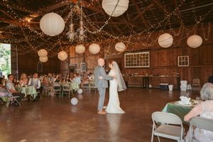 Wedding ceremony in a rustic barn reception venue decorated with white paper lanterns and twinkling string lights.