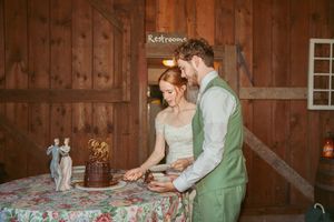 Couple cutting their wedding cake together in a rustic wooden barn setting.