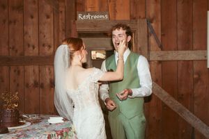 A couple sharing a playful moment while cutting their wedding cake in a rustic barn setting.