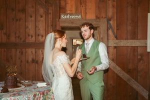 Couple sharing cake at rustic barn wedding reception with wooden wall backdrop.