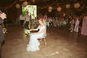 Wedding reception in a rustic barn venue decorated with paper lanterns and string lights while a seated bride awaits guests.