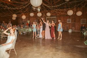 Wedding guests dancing and celebrating in a barn venue decorated with string lights and paper lanterns.