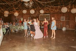 Wedding reception party inside rustic barn decorated with string lights and paper lanterns during evening celebration.