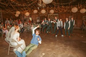 Guests dancing and having fun at rustic barn wedding reception under twinkle lights and paper lantern decor.