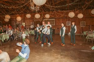 Wedding guests dance on the rustic barn floor decorated with string lights and paper lanterns overhead.