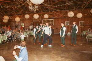 Groomsmen performing a choreographed dance routine at a barn reception under warm string lights.