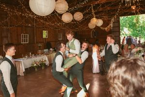 Playful groomsmen lifting and carrying someone during a lively dance at a barn wedding reception.