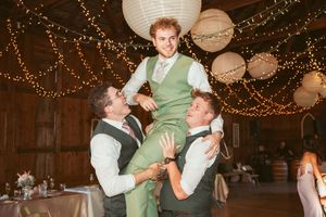 Celebratory moment as groomsmen lift someone up during a wedding reception in a decorated barn venue.