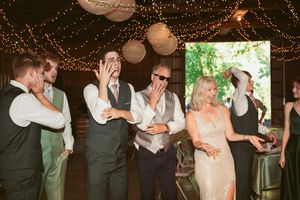 Wedding party dancing and celebrating together inside rustic barn reception with string light decorations.