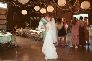 A couple shares their first dance at a rustic barn wedding reception decorated with white paper lanterns and string lights.