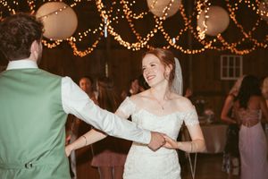 Joyful couple sharing their first dance in a barn venue illuminated by warm string lights.