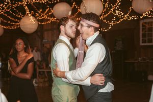 Couples dance and celebrate during a festive barn wedding reception under warm lighting.