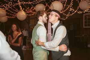 Two people embrace on a dance floor decorated with string lights and paper lanterns at a wedding reception.