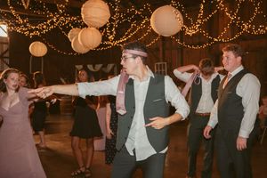 Guests dancing and having fun under warm string lights at a rustic venue celebration.